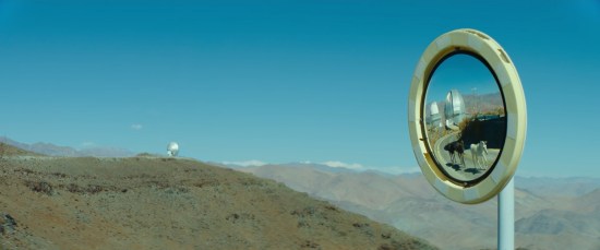 Small, round mirror sticking up in the middle of a desert. Visible onlyin the mirror are three donkeys and an observatory.