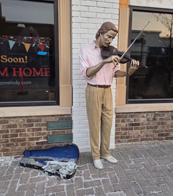 Statue of busking violinist. Open case on sidewalk has sculpted dollar bills thrown in.