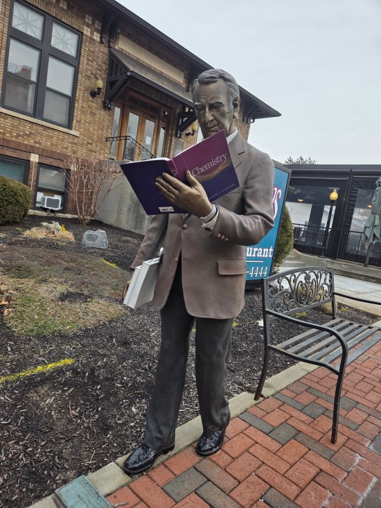 Statue of 1960s professor reading a chemistry book and not watching where he's walking.