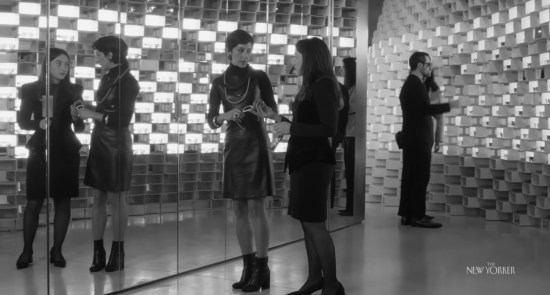 Shopgirl and shopper in black-and-white shoe store with one wall made of light-up shoeboxes and a floor-to-ceiling mirror on the other side.