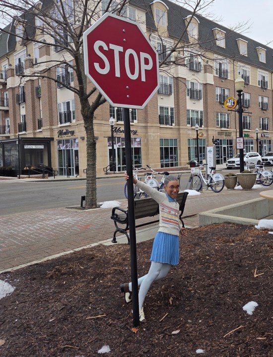 statue of little Black girl swinging from a real stop sign. In the background are very nice apartments.