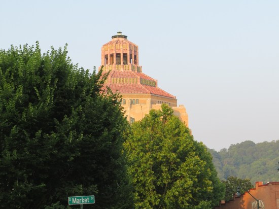 Asheville City Hall looks like a stone temple, lit by the sunset, shrouded by trees, green mountains in the distance.
