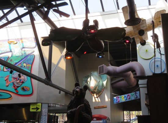 Restaurant wall decor includes a large propeller fan, a carved standing bear, a mounted cartoon elephant head, and a big model biplane.