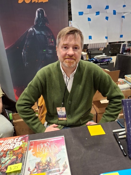 Charles Soule at his C2E2 table, Darth Vader banner behind him and copies of The Lucky Devils on his table.