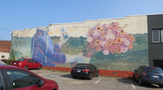 Mural of a guy among green mountains, holding a giant bouquet in one hand and a baseball-sized dandelion in the other.