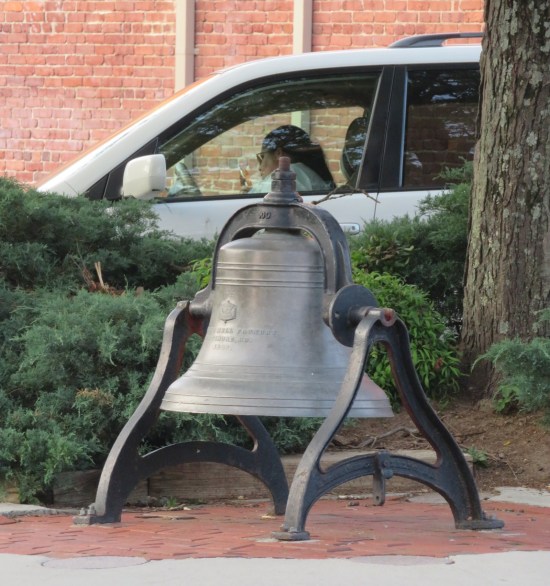 Big bell sculpture on a stand on a brick sidewalk. Inscription says it was made in Baltimore. It's not cracked.