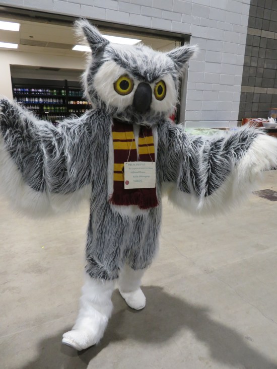 adult in giant white owl costume with Gryffindor scarf and large envelope hanging around neck, addressed to Harry Potter's place.