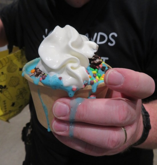 Cup overfilled with two scoops of chocolate ice cream and blue topping, melting over the sides and dripping all over my hand.