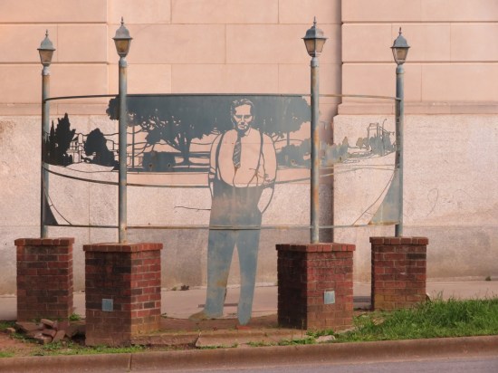 6-foot 2-D metal sculpture of a lawyer in tie and suspenders, hands in pockets, standing in front of a thin metal backdrop.