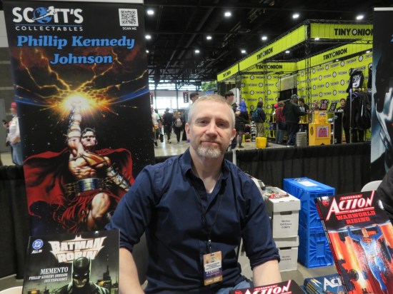 Phillip Kennedy Johnson at his C2E2 booth, with images of Batman and Superman around him. Covering much of the background is the large, very yellow Tiny Onion booth.
