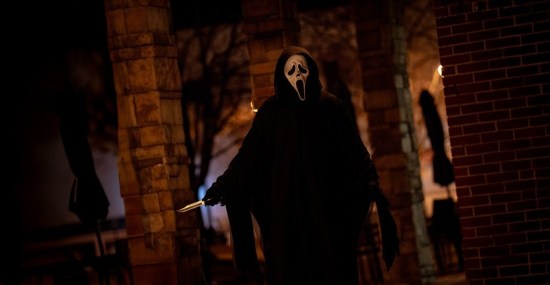 Ghostface walks past the side of a brick coffee shop, knife in hand, mask yawning.