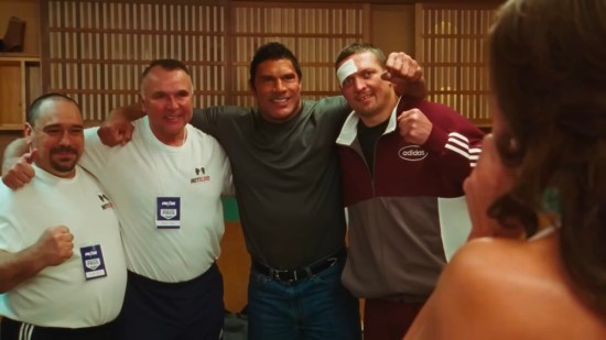 The Rock unrecognizable in heavy makeup, posing for photo with three other smiling guys.