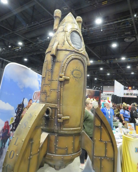Large steampunk rocketship model at a con booth.