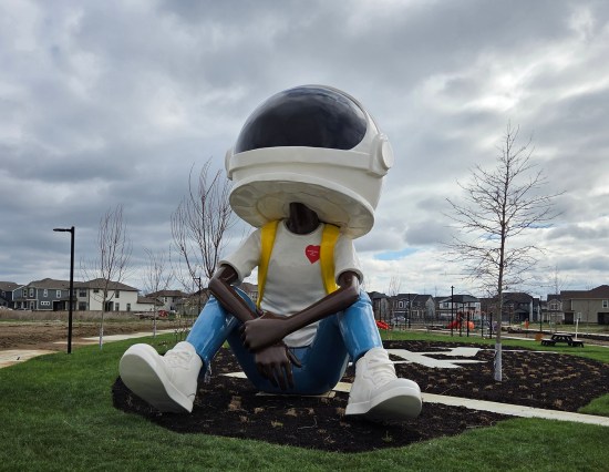 25-foot statue of a Black boy wearing an astronaut helmet, sitting in a city park and gazing toward the sky.