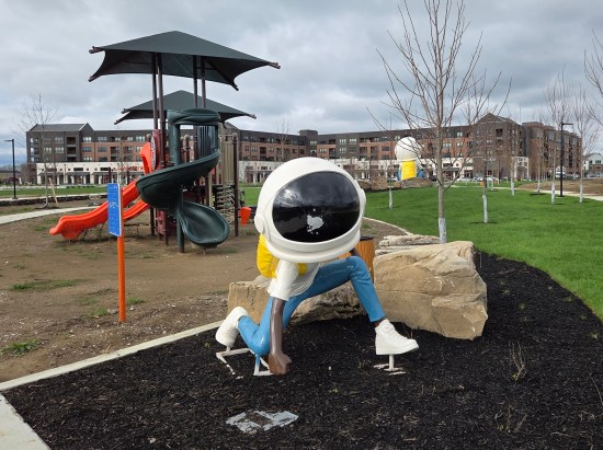 Black astronaut kid statue in a playground, posed like he's just made an Iron Man-style hard landing after flying.