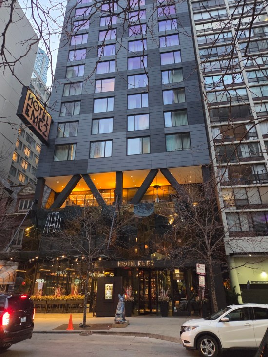 All-black skyscraper hotel. Small trees along the front sidewalk haven't sprouted new leaves yet.