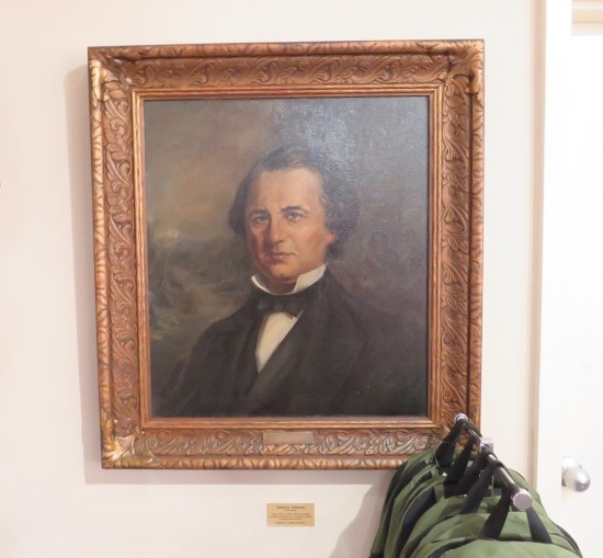 Painting of Andrew Johnson hung above a rack of Andrew Johnson green backpacks.