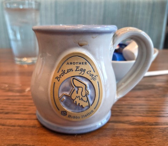 White coffee mug with Another Broken Egg logo and chicken head image inside an egg-shaped border titled "US 40 Hobbs Station".