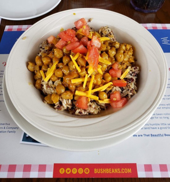 Bowl of beans, rice and quinoa topped with diced tomatoes and shredded cheese.