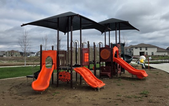 Black and orange playground equipment with black canopies, including at least four slides. Parts are decorated with the alphabet and a lesson about insects.