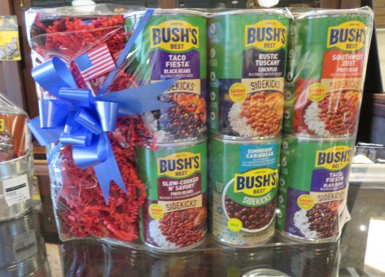 Six cans of Bush's Sidekicks beans, each one a different flavor, wrapped in plastic with a blue gift bow on top.