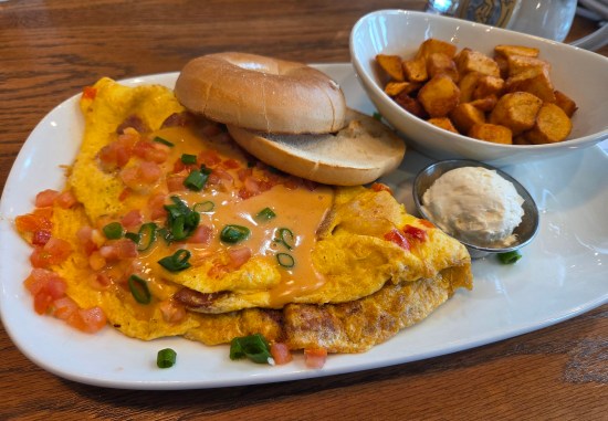 omelet with shrimp, crawfish, orange sauce, diced tomatoes, and green onions. Sides are country potatoes and a plain bagel with butter.