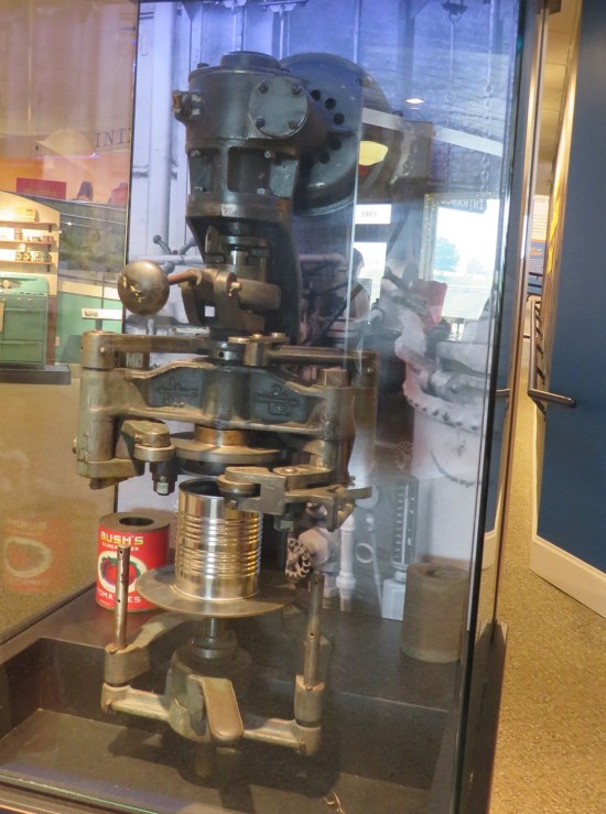 Overly complicated 20th-century machine with a can mounted near the bottom, all behind glass.