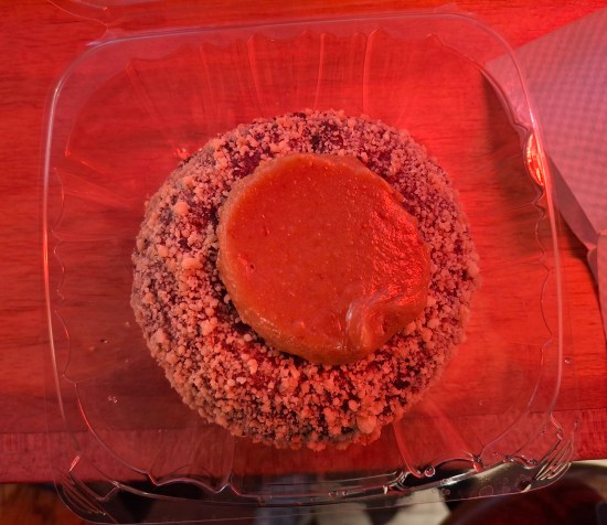 A very red cake donut with red icing, and somehow the lighting also turned red.