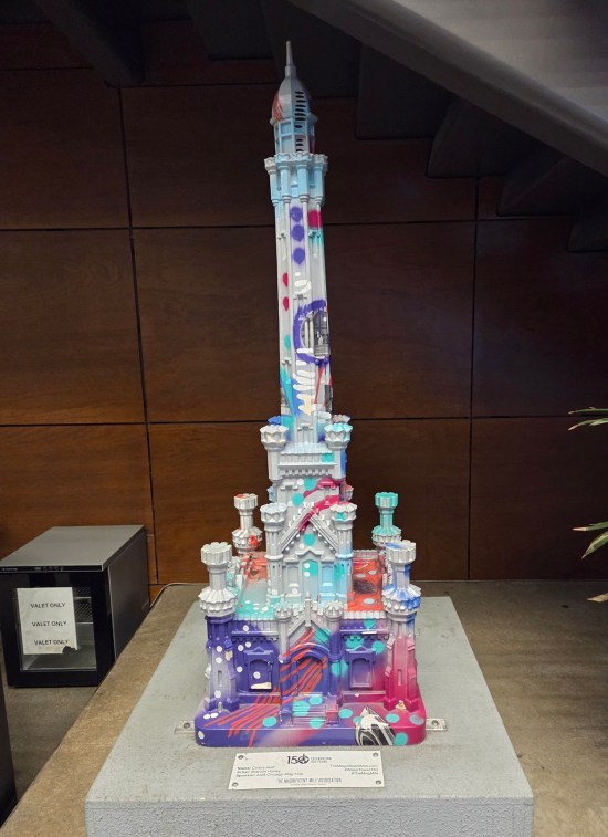 Sculpture of a church-like old structure with a high minaret and multiple towers near the bottom. Sculpture is mostly white with random accents of purple, light blue and red.