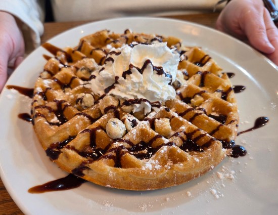 waffle topped with small cookie dough balls, chocolate syrup, a touch of powdered sugar and a dollop of whipped cream.