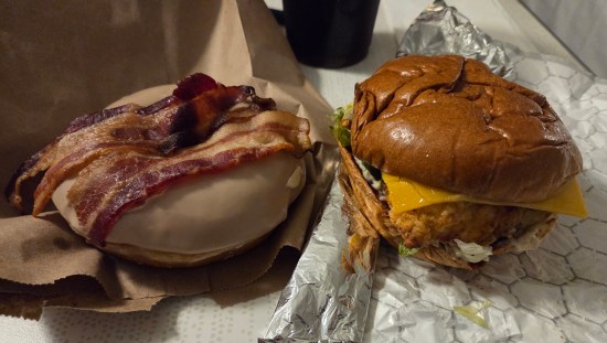 A maple iced donut topped with a slice of bacon and a fried chicken sandwich.