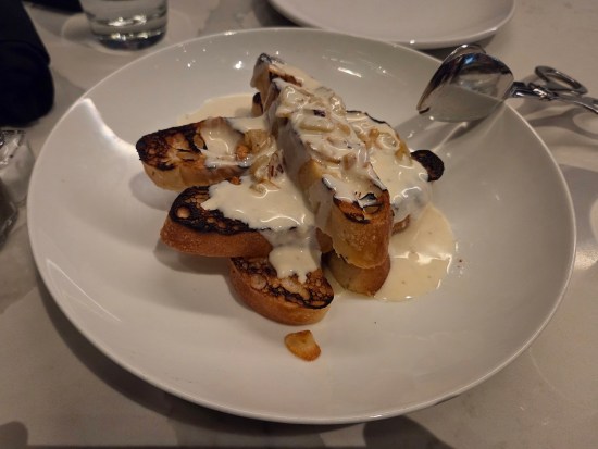 Five oblong slices of garlic bread stacked on a plate and covered in white sauce.