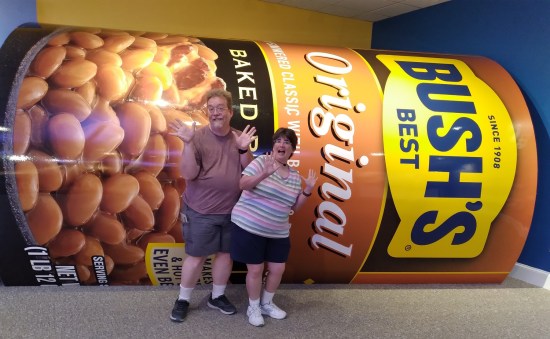 Us in summer wear doing jazz hands in front of a giant prop can of Bush's Baked Beans, lying on its side in a visitor center.