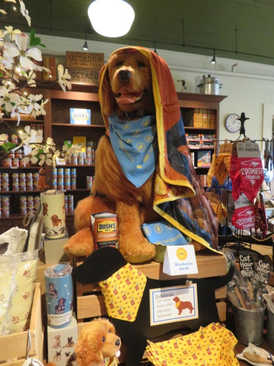 Life-size Duke doll sitting on a gift shop table with random items around him.