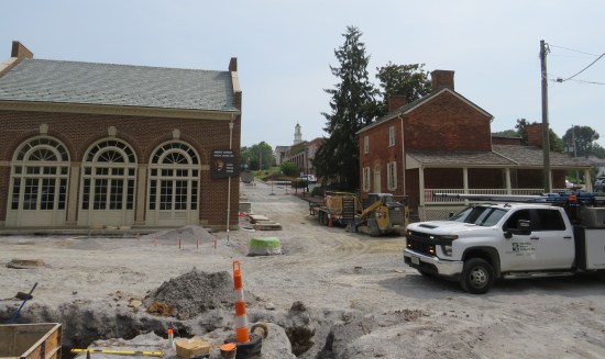 Old brick buildings with an Andrew Johnson National Historic Site sign out front, but the streets have been scraped down to dirt and gravel. An equipment pit is at far left.