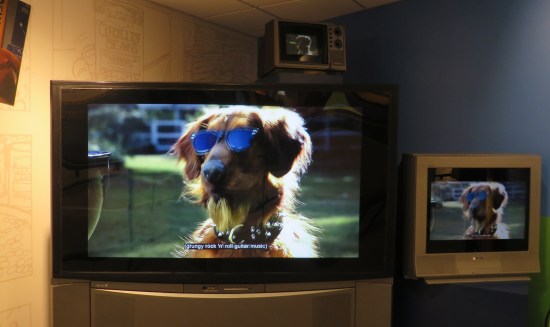 Three TVs showing Duke the dog wearing sunglasses with the bracketed closed caption "grungy rock 'n' roll guitar music".