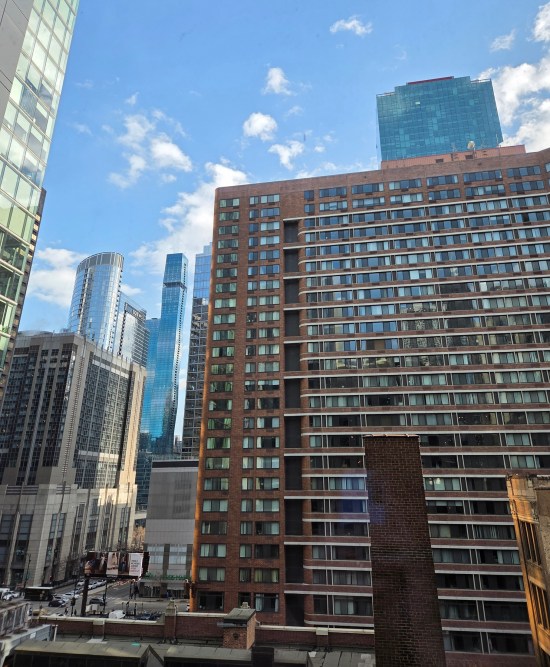 downtown Chicago skyscrapers in daylight. One of them has a Whole Foods on the ground floor. Sky is blue with a few small puffy clouds.