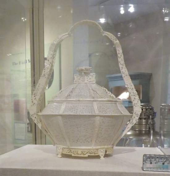 Elegant ivory basket with handle, in a museum case with thermometer in the corner.