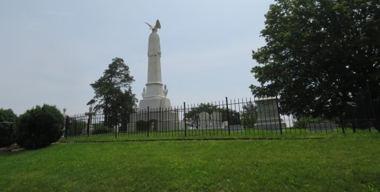 Side view of fenced plot of graves atop a hill, with a large obelisk in the middle of them.