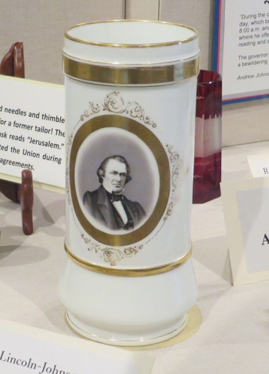 White cylindrical vase with gold trimmings and a drawing of Andrew Johnson.