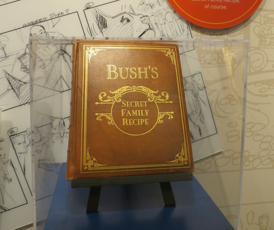 Large fake brown hardcover book labeled "Bush's Secret Family Recipe" in a museum vitrine.