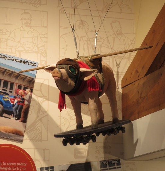 pig statue hanging from the ceiling with wooden wings, aviator mask, red scarf and skateboard.