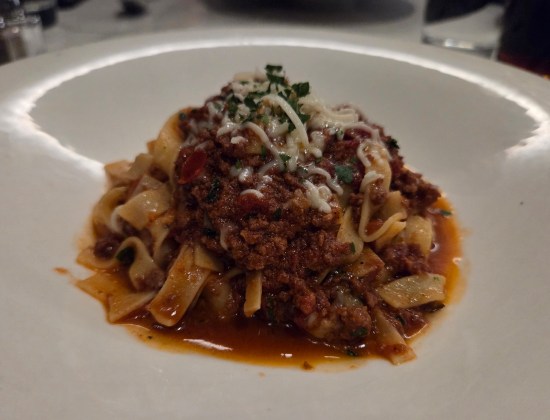 Small serving of beef and noodles with white cheese strands and a few herbs on top.