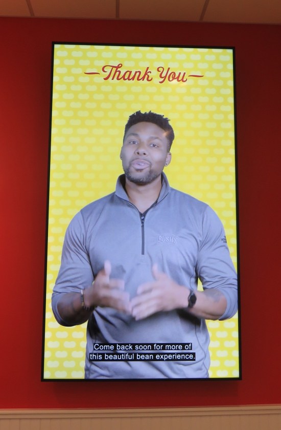 Vertically hung TV on a red wall. Black male narrator with closed caption "Come back soon for more of this beautiful experience." Above his head are the words "Thank you".