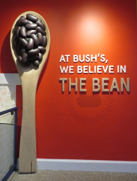 Red wall with a giant wooden spoon standing on end, containing beans. Wall motto is "At Bush's, we believe in the bean."