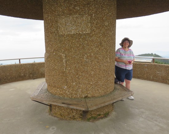 Anne on an observation deck next to a beige stone column as wide as four humans, with wooden benches built into and around it.