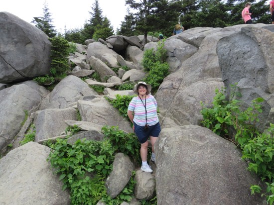 Anne standing next to piles of giant rocks. Other tourists walk around the level above them.