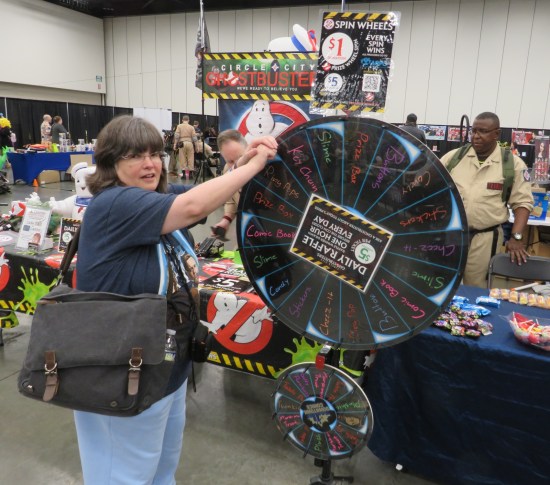 Anne spins a wheel listing prizes such as key chain, slime, prize box, ring pop, comic book, and more.