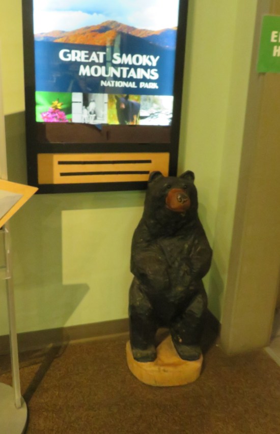 carved black bear in the corner of a gift shop with green walls and a flat monitor.