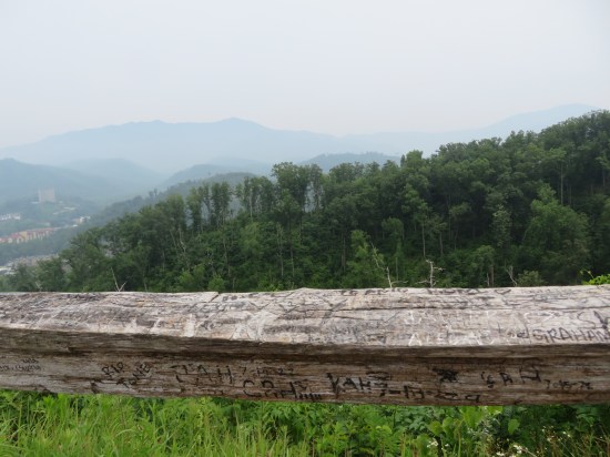 wooden railing around an overlook with more initials carved into it. Beyond lay forests and Gatlinburg.